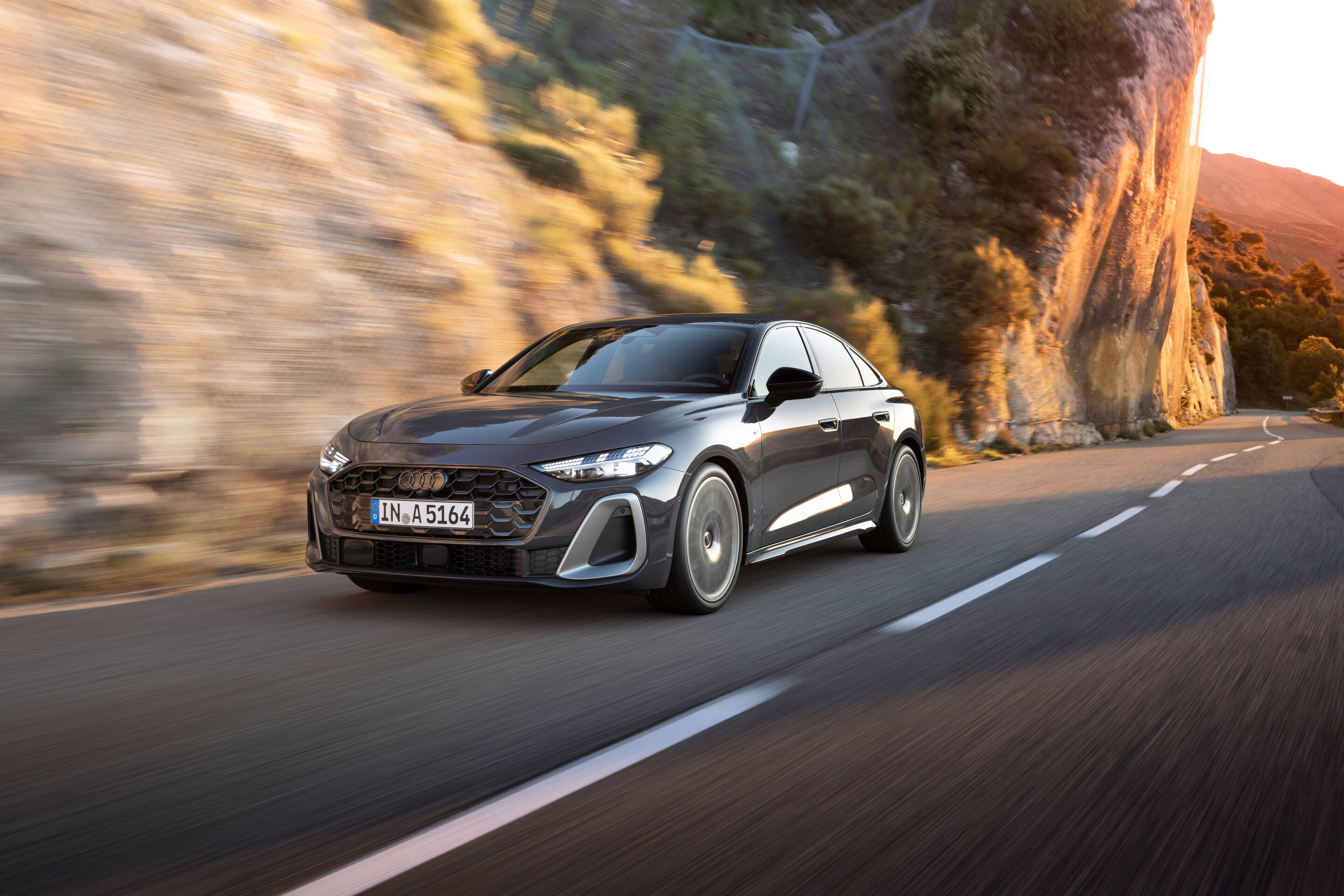 Audi A5 Sedan - An Audi A5 Sedan drives along a coastal road. Steep cliffs can be seen in the background. The vehicle is painted in Magnet gray.