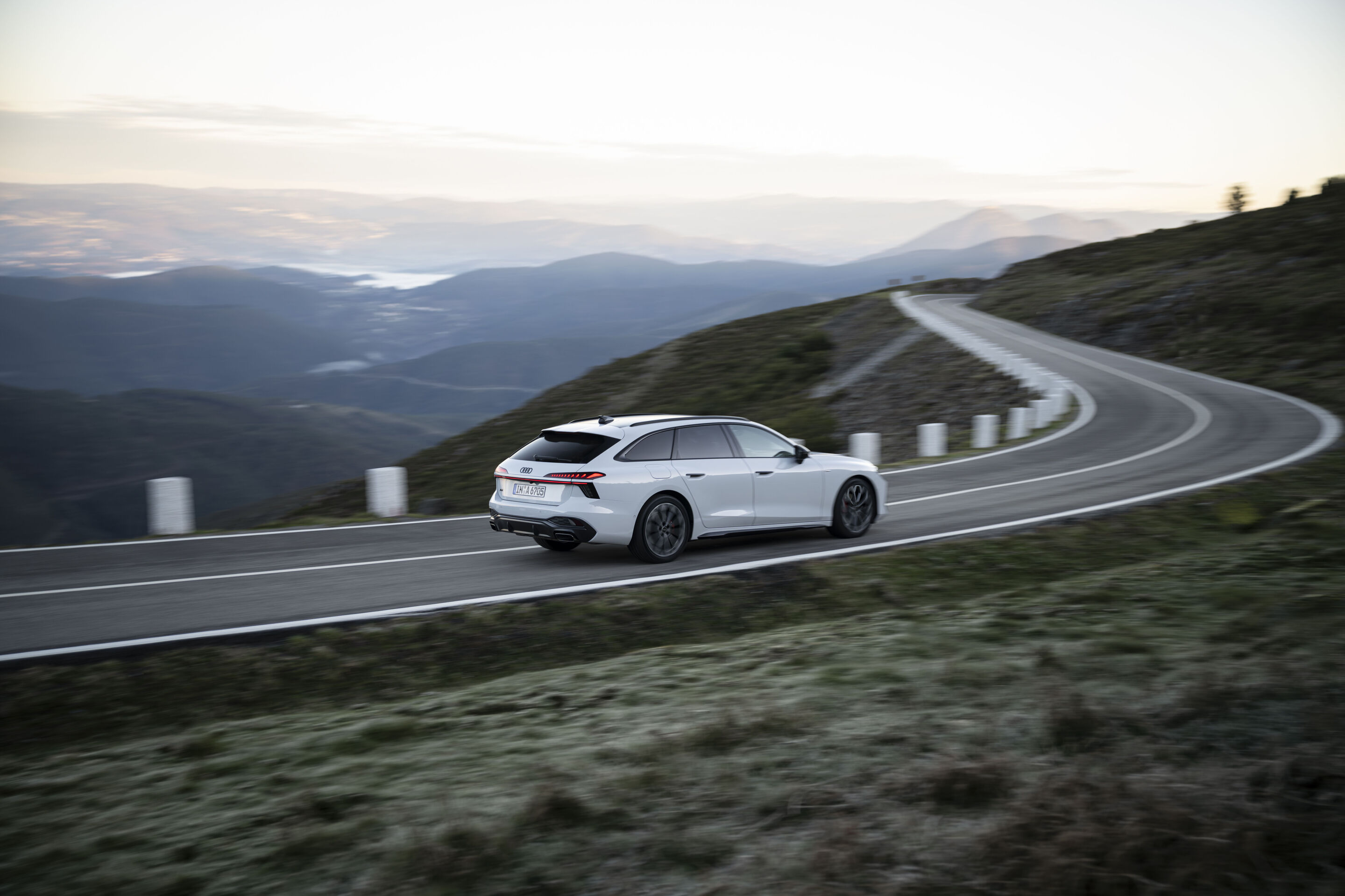 Connected development: the Audi A6 Avant as the perfect travel companion - An Audi A6 Avant in Glacier White Metallic drives along a winding mountain pass. The horizon lies in the background.